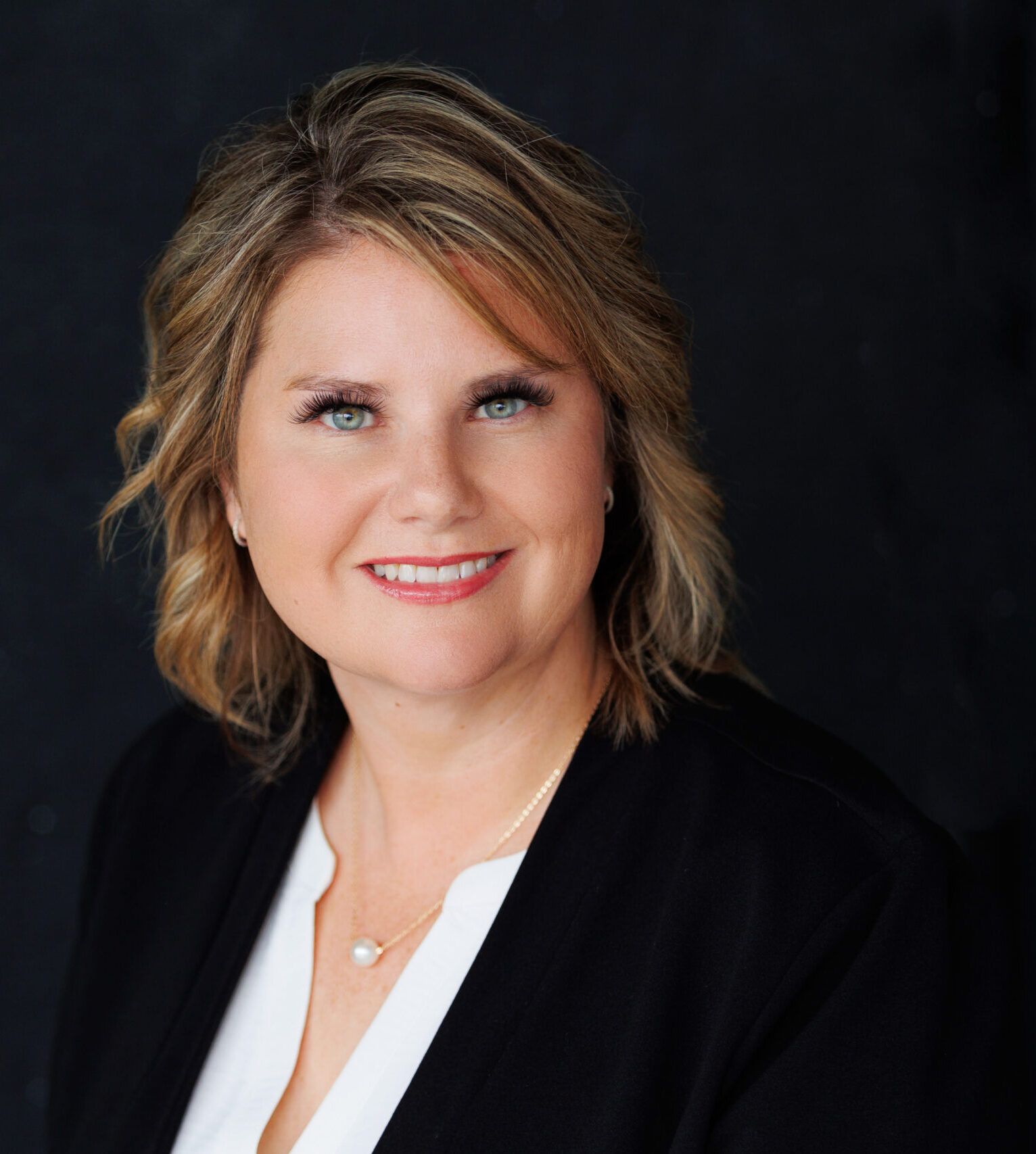 amy 104 Smiling woman in professional attire with dark background.