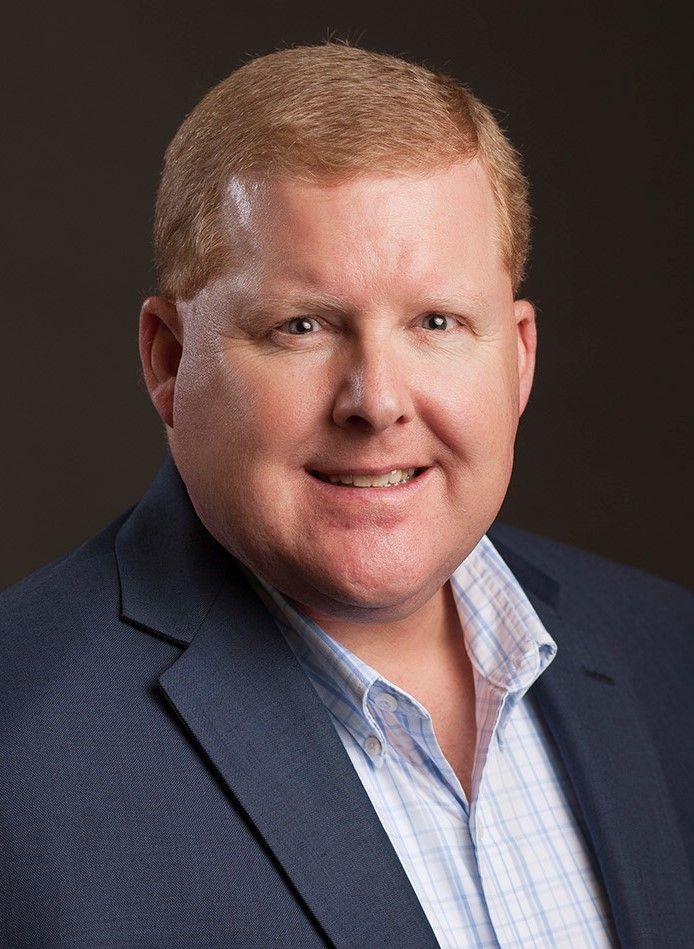 clintwiles (2) Person in suit smiling against dark background